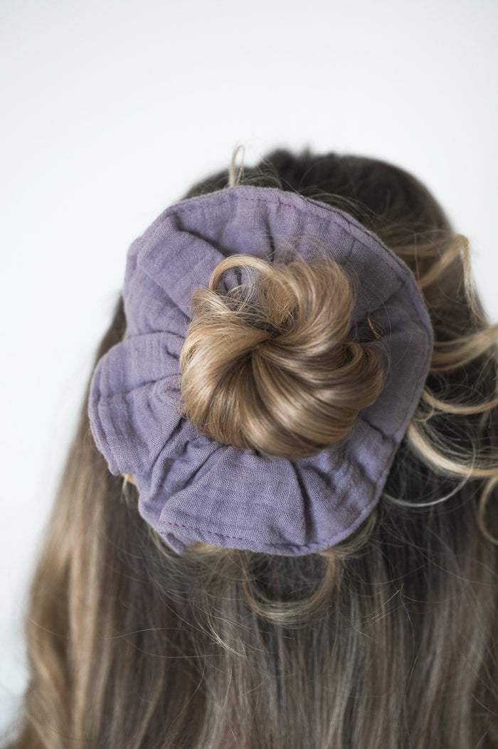 Chouchou violet en gaze de coton, attaché dans les cheveux d'une personne avec un chignon bas